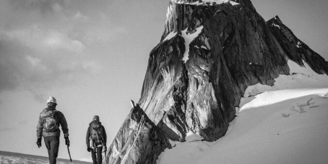 grayscale photo of two people walking on mountain valley