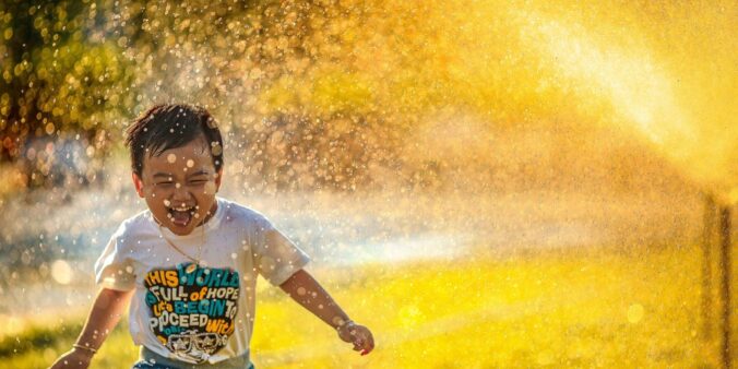 a young boy running through a sprinkle of water